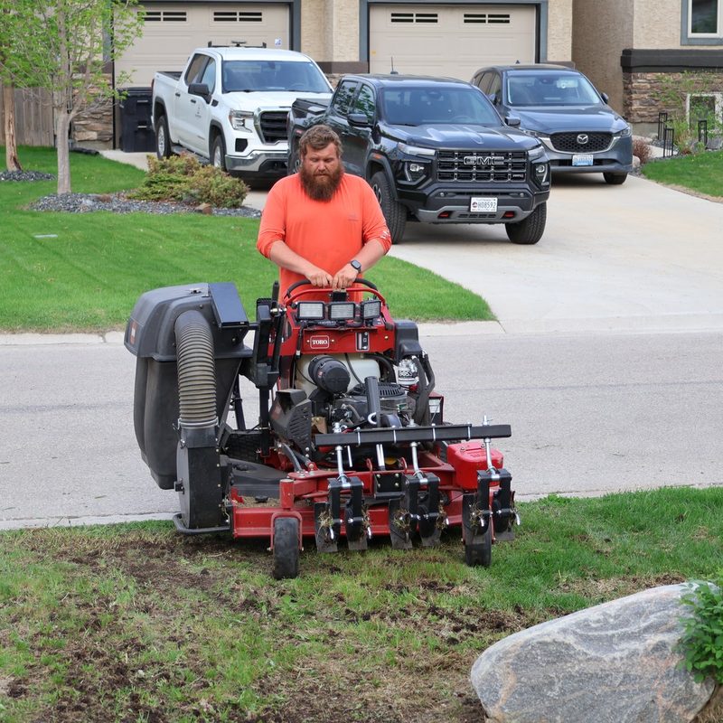 A GoYardly crew member operating a Toro stand-on dethatcher at a Selkirk-area property